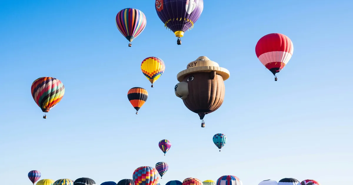 Dozens of colorful hot air balloons rising over a crowd at a mass launch