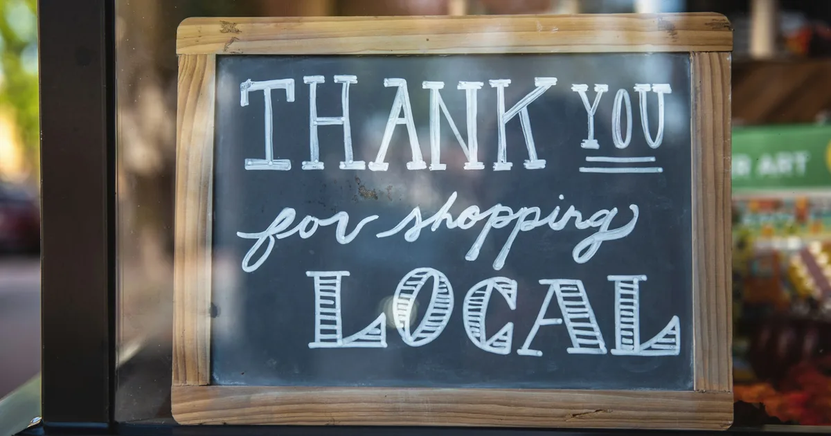 Chalkboard sign in a shop window reading Thank You for Shopping Local