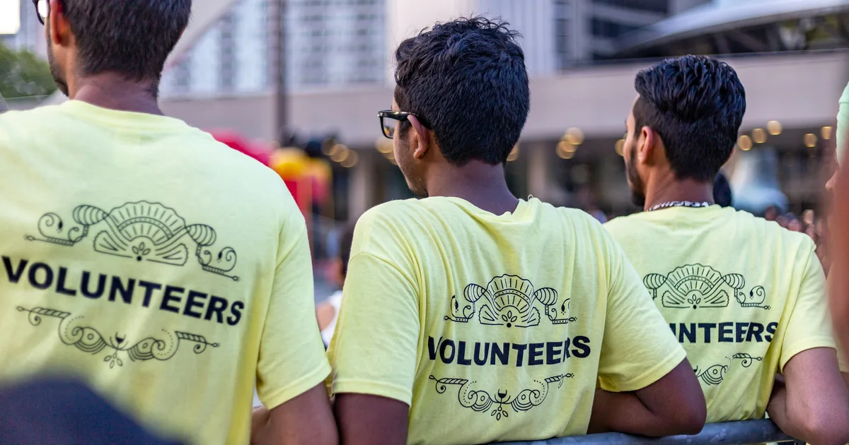 Three volunteers seen from behind wearing matching yellow t-shirts printed with the word Volunteers