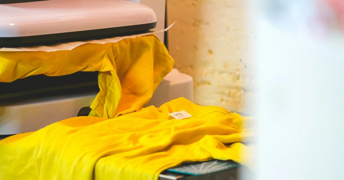Heat press machine applying a transfer to a yellow t-shirt during the curing step of a DTF workflow