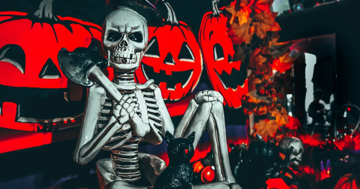 Halloween skeleton decoration holding an axe beside a black cat figurine and glowing jack-o'-lantern displays