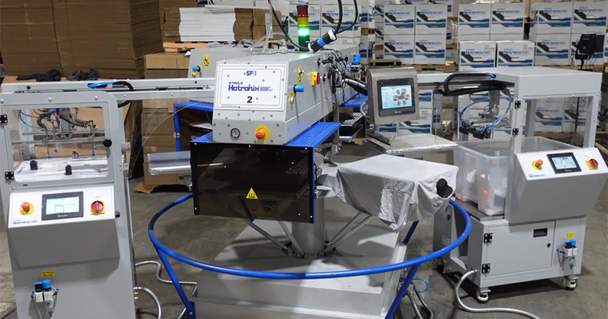 Hotronix Carousel rotary heat press with its central press head, blue rotating platen ring, auto placer, and auto peeler units on a warehouse floor