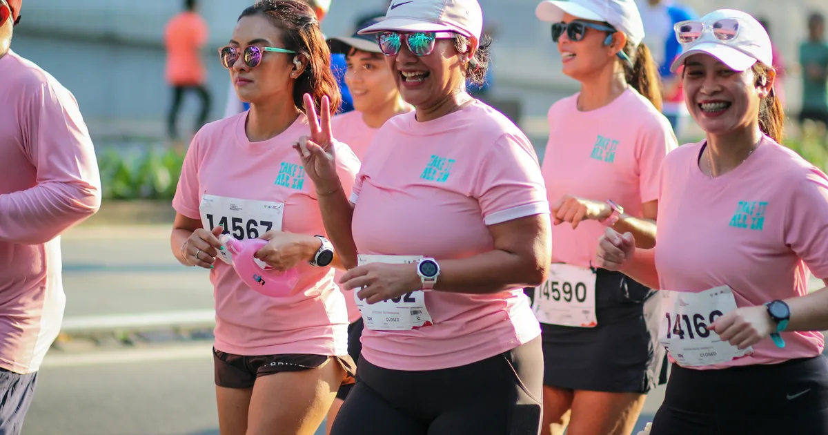 Women running a road race in matching pink event t-shirts with race bibs pinned on